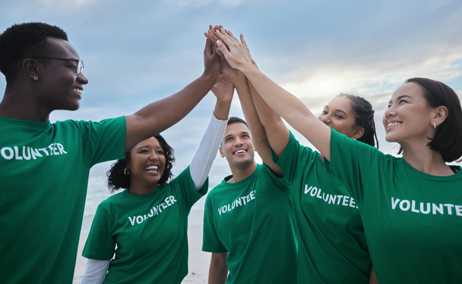 Teamwork, high five and volunteer with people on beach for sustainability, environment and climate change. Charity, earth day and community with friends for support, diversity and pollution awareness